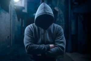 dangerous criminal. scary hooded man at night in dark alley. silhouette bandit, criminal with an unrecognizable face in threatening pose at night on dark street. Mysterious man in silhouette